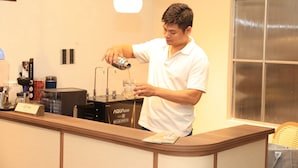 Eine Person gießt ein Getränk in ein Glas an einer Theke mit einer Kaffeemaschine und einem Wasserspender.