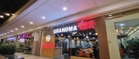 A restaurant named 'GRANDMA' with a neon sign, located in a shopping mall.