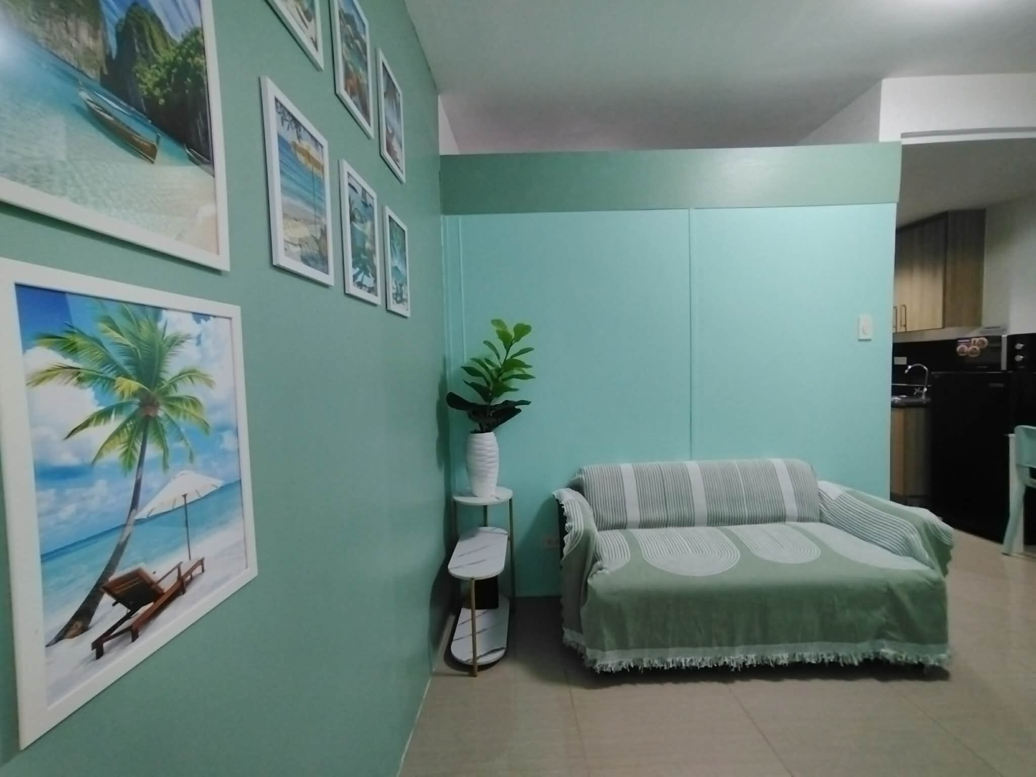 A living room with a sofa, a small table, and a plant. There are framed pictures on the wall.