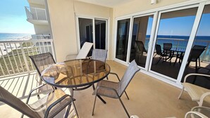 En balkon med et glasbord og stole, der giver udsigt over en strand og et hav.
