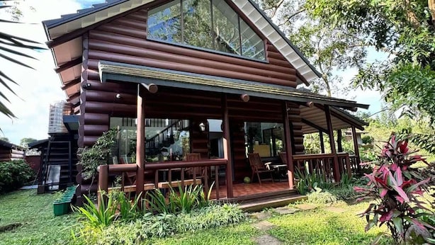 A wooden cabin with a covered porch, a small garden, and a staircase leading to the entrance. - Luntian Log cabin in Tagaytay (Tagaytay City)