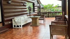 A wooden deck with a white sofa, wicker table, and wooden chairs. - Luntian Log cabin in Tagaytay (Tagaytay City)
