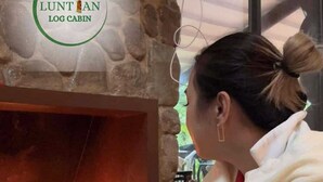 A person sitting by a stone fireplace with a visible logo above it. - Luntian Log cabin in Tagaytay (Tagaytay City)