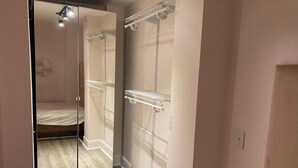 Une pièce avec une porte de placard miroir, un lit et une étagère blanche.