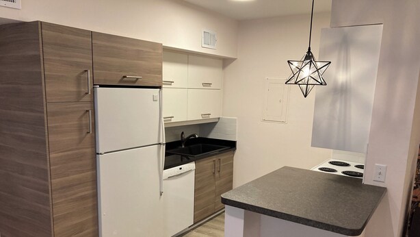 Une cuisine compacte équipée d’un réfrigérateur, d’une cuisinière, d’un évier et de meubles de rangement en bois.