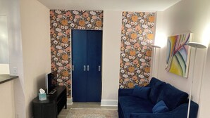 Une pièce avec une porte bleue, un canapé bleu, un lampadaire et un tapis à motifs.