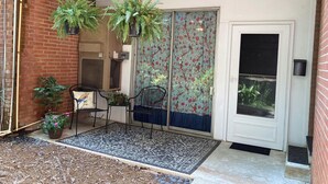 Une terrasse couverte avec un mur en briques, deux chaises, une petite table et des plantes suspendues.