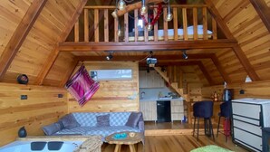 Una cabaña acogedora de madera con un dormitorio en el altillo, cocina y sala de estar, además de un jacuzzi y alfombras de colores.