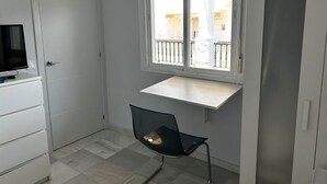 A small, clean room with a white door, a TV on a white cabinet, a window with a balcony view, and a black chair. - Central Studio Penthouse very close to the beach. Large terrace. (Rota)