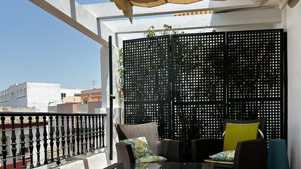 A balcony with a black wicker sofa, a glass coffee table, and a black perforated screen. - Central Studio Penthouse very close to the beach. Large terrace. (Rota)