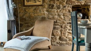 Une pièce chaleureuse avec un mur en pierre, une chaise en bois, une table avec un bol, et un tableau encadré accroché au mur.