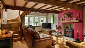 Un salon chaleureux avec un canapé en cuir, un escalier en bois, une cheminée et un téléviseur.