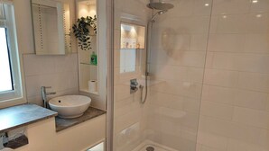 Ein modernes Badezimmer mit einem weißen Waschbecken, einer Glasdusche und einem Spiegel über dem Waschbecken.