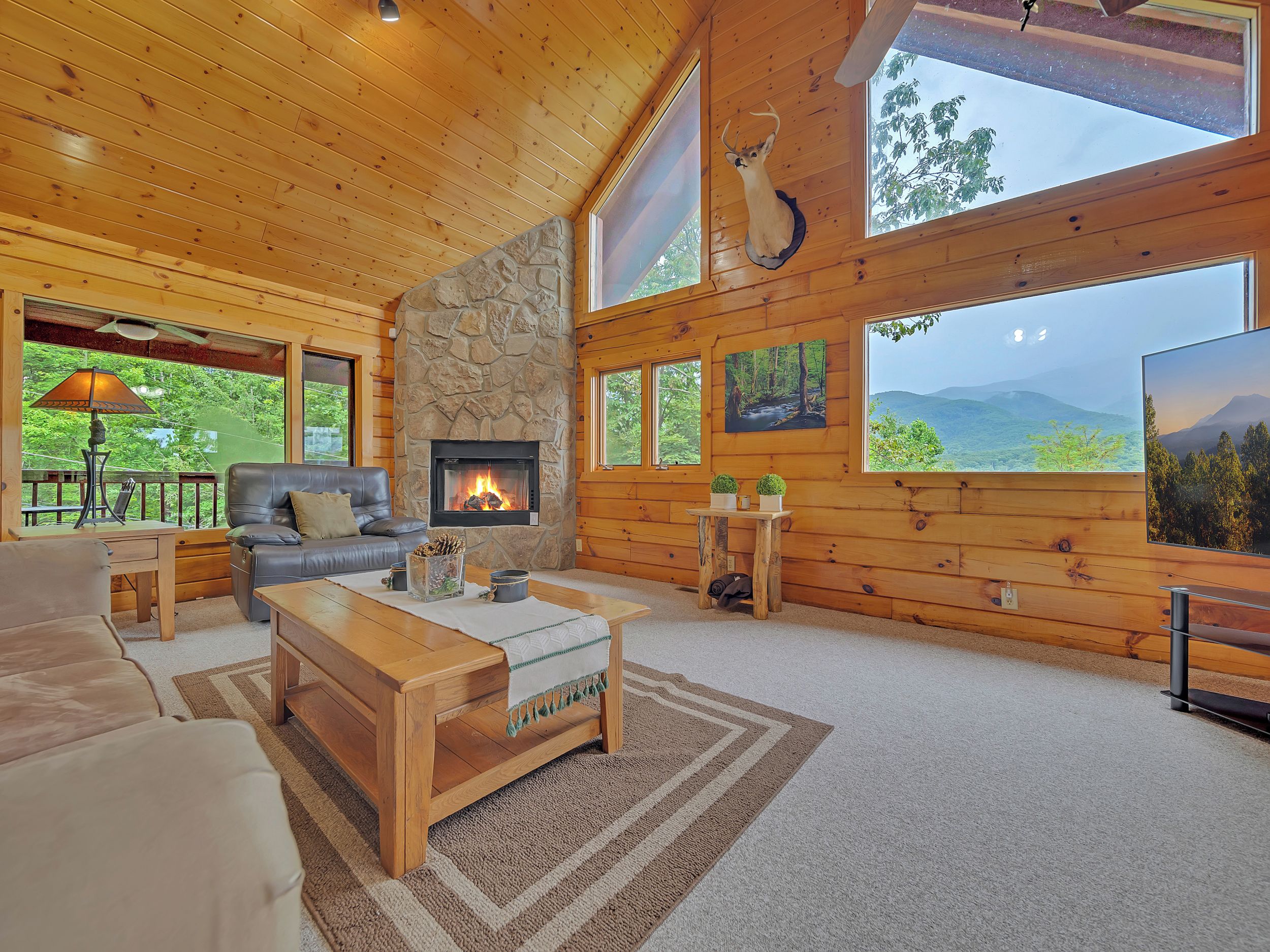 Interior acogedor de una cabaña con chimenea de piedra, paredes de madera, un sofá de cuero, una mesa de centro y grandes ventanales con vistas panorámicas.