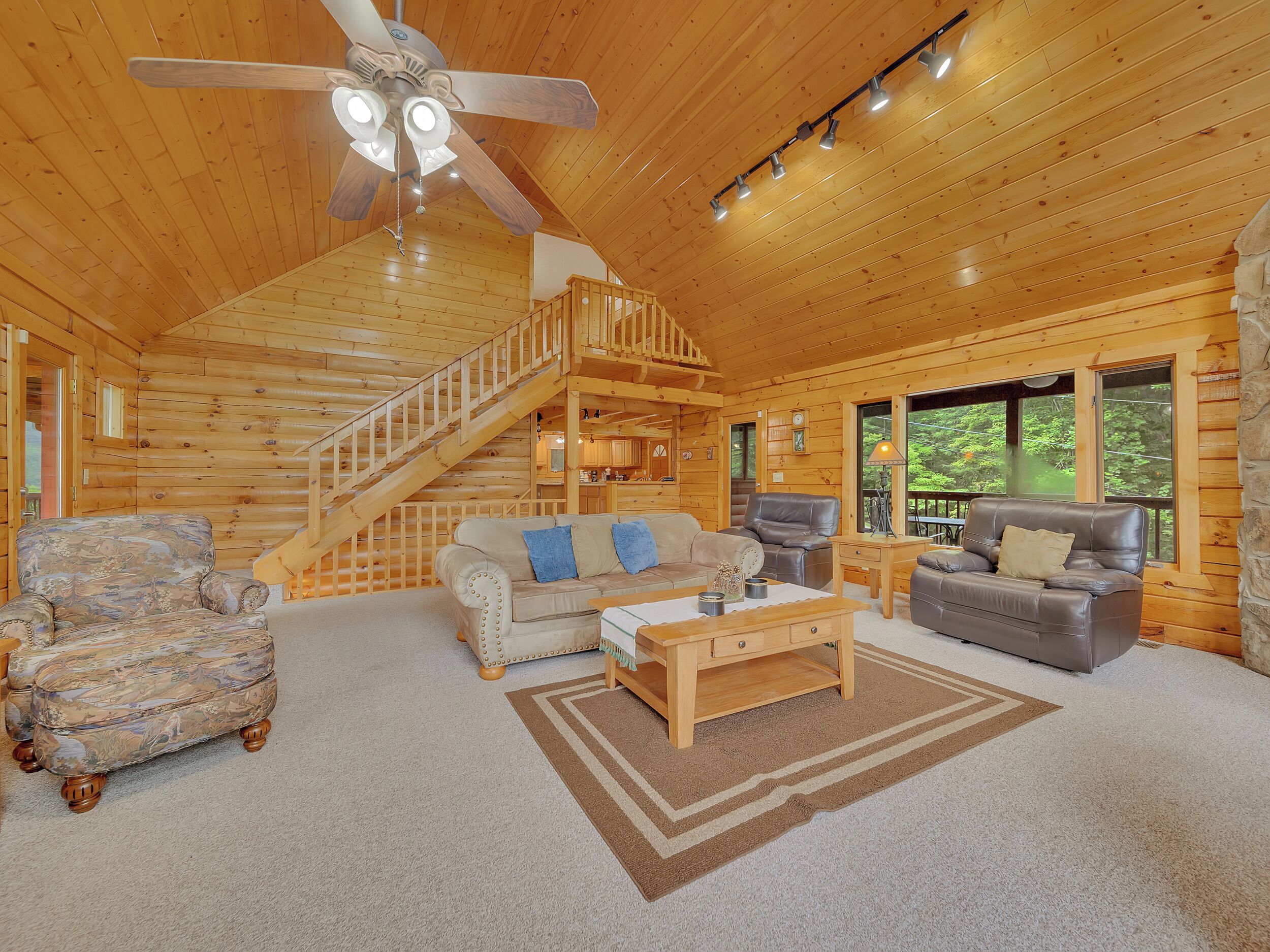 A log cabin interior with a wooden staircase, a sofa, a leather chair, and a coffee table.