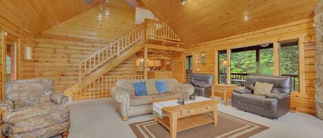 A log cabin interior with a wooden staircase, a sofa, a leather chair, and a coffee table.