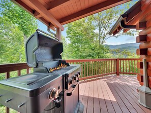 Una parrilla de barbacoa en una terraza de madera con vistas a un bosque y montañas.