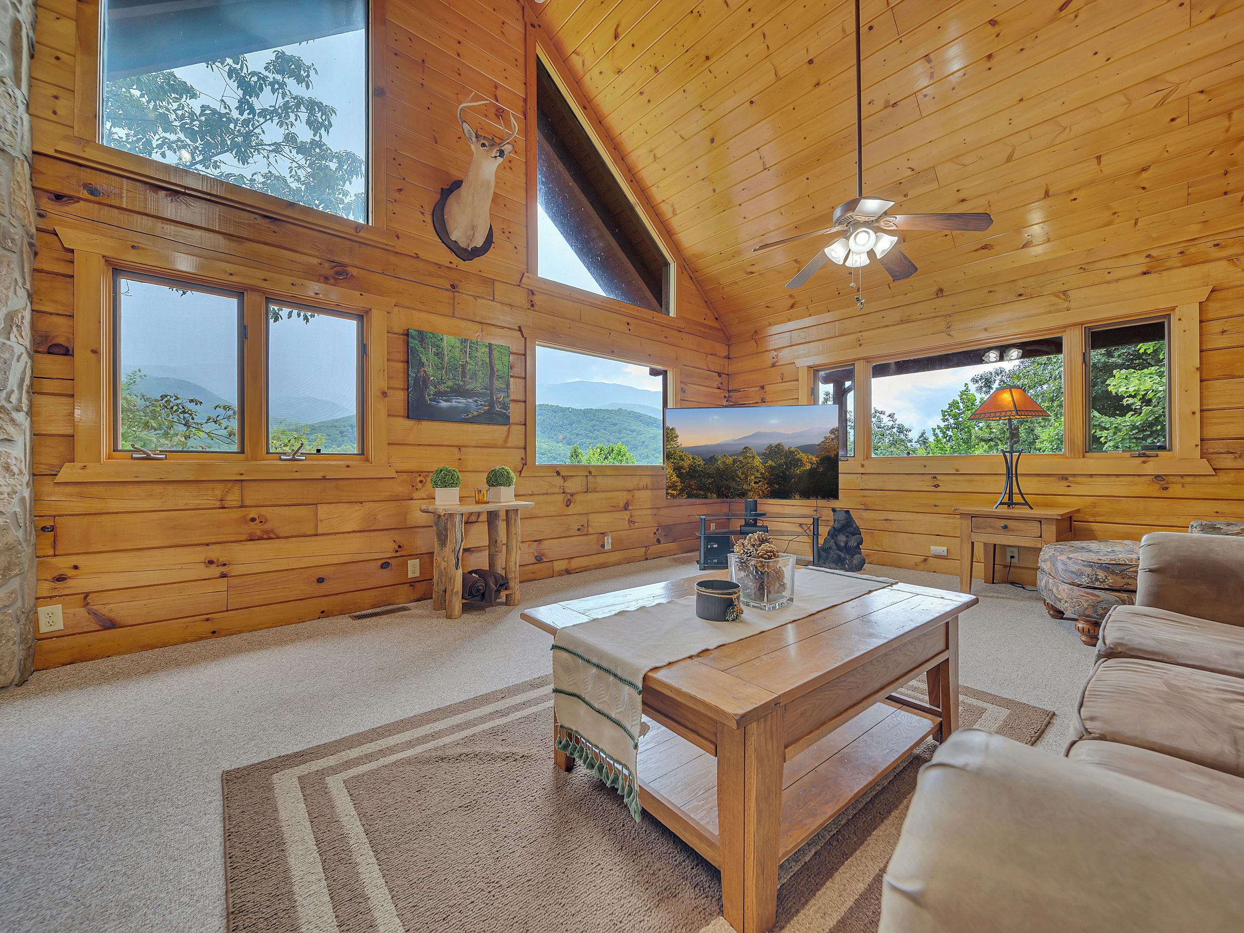 A cozy cabin interior with wooden walls, a ceiling fan, a large TV, a wooden coffee table, and a sofa.