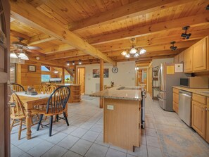 Interior de una cabaña de madera con comedor, cocina y una pequeña isla con refrigerador y microondas.