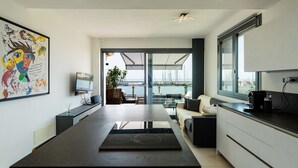 Eine moderne Küche mit einer großen Kochinsel, ein Essbereich mit Blick auf den Yachthafen und ein Wohnbereich mit einer Couch und einer Kaffeemaschine.