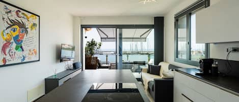 A modern kitchen with a large island, a dining area with a view of the marina, and a living area with a sofa and a coffee machine.