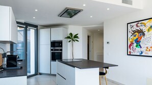 Eine moderne Küche mit weißen Schränken, einer schwarzen Arbeitsplatte und einem Barhocker. Ein großes Fenster lässt natürliches Licht herein und bietet einen Ausblick nach draußen.