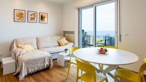 Un salon moderne avec un canapé, une table ronde, des chaises jaunes et un balcon offrant une vue dégagée.