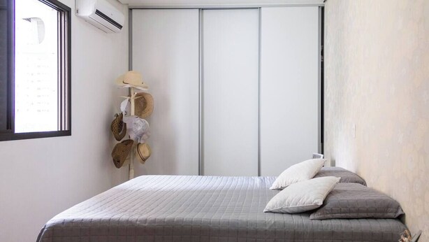 A bedroom with a bed, pillows, a bedside table with glasses, and a wall-mounted air conditioner. - 3 bedroom apartment, Pitangueiras Beach, Guarujá (Barra Funda Guarujá)