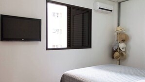 A bedroom with a bed, a wall-mounted TV, a window with blinds, and a wall-mounted air conditioner. - 3 bedroom apartment, Pitangueiras Beach, Guarujá (Barra Funda Guarujá)