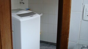 A compact laundry room with a washing machine, a sink, and a small countertop. - 3 bedroom apartment, Pitangueiras Beach, Guarujá (Barra Funda Guarujá)