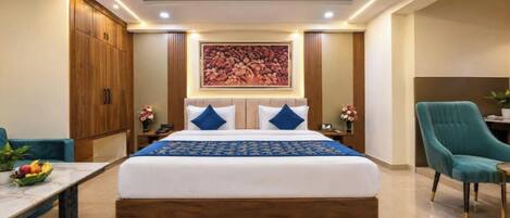 A hotel room with a large bed, a desk, a chair, and a wardrobe.