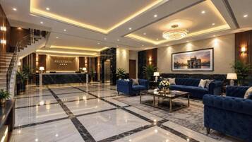 A hotel lobby with a reception desk, a staircase, and a seating area with sofas and a coffee table.