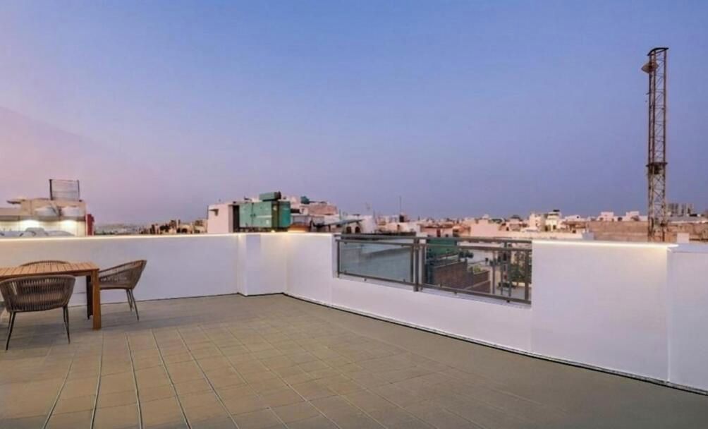 A rooftop terrace with a view of the cityscape, a table with chairs, and a tall communication tower.