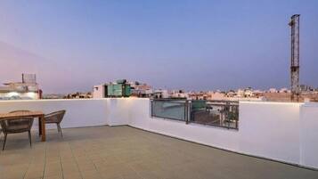A rooftop terrace with a view of the cityscape, a table with chairs, and a tall communication tower.
