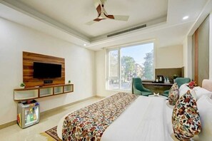 A hotel room with a bed, a desk, a television, a window, and a ceiling fan. - Hotel Dream World (New Delhi)