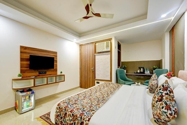 A hotel room with a bed, a television mounted on the wall, a minibar, a ceiling fan, and a seating area with chairs. - Hotel Dream World (New Delhi)