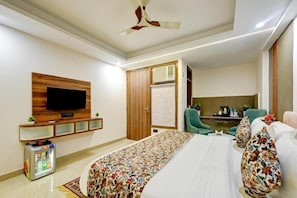 A hotel room with a bed, a television mounted on the wall, a minibar, a ceiling fan, and a seating area with chairs. - Hotel Dream World (New Delhi)