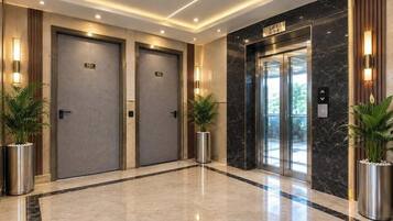 A modern hotel lobby with two elevators, marble flooring, and potted plants.