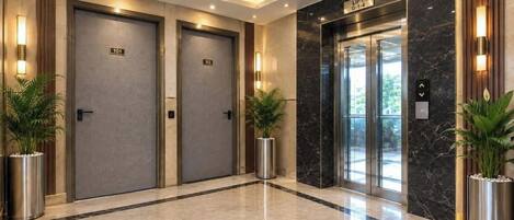 A modern hotel lobby with two elevators, marble flooring, and potted plants.