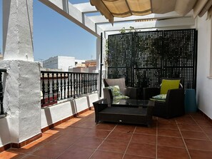 Un balcon agrémenté d’un canapé en osier, d’une table en verre et d’un paravent décoratif.