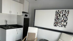Una cocina moderna con armarios blancos, encimera negra y microondas. Hay dos sillas color beige con estructura de madera y una mesa redonda pequeña. En la pared, una obra de arte abstracta de gran tamaño.