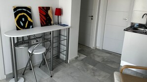 Una cocina compacta con encimera blanca, un fregadero y una puerta que da a otra habitación.