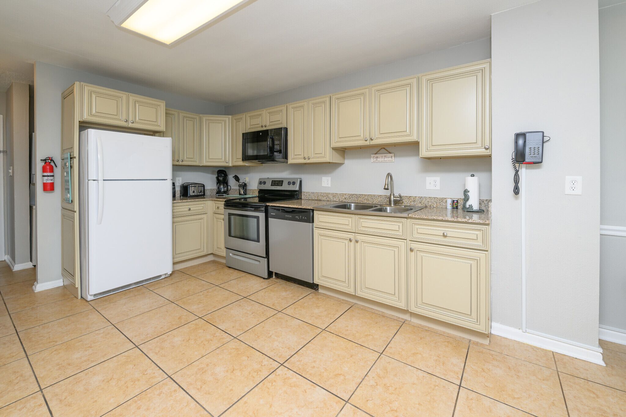 A kitchen with beige cabinets, a white refrigerator, a microwave, a stove, a dishwasher, and a phone on the wall.