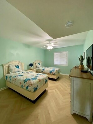 A bedroom with two beds, a ceiling fan, a window with blinds, and a nightstand with a lamp.