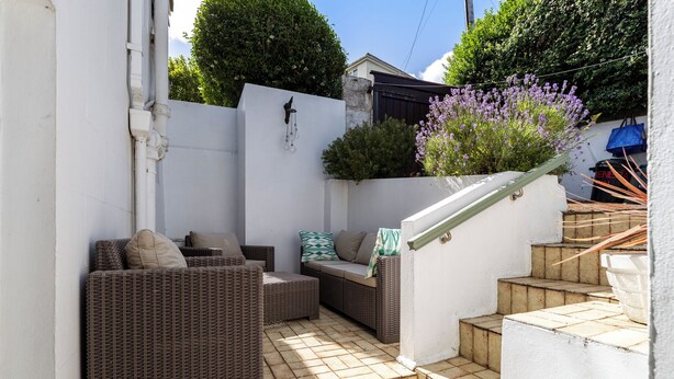 Un espace patio aménagé avec des meubles en osier, un mur blanc et un petit escalier.