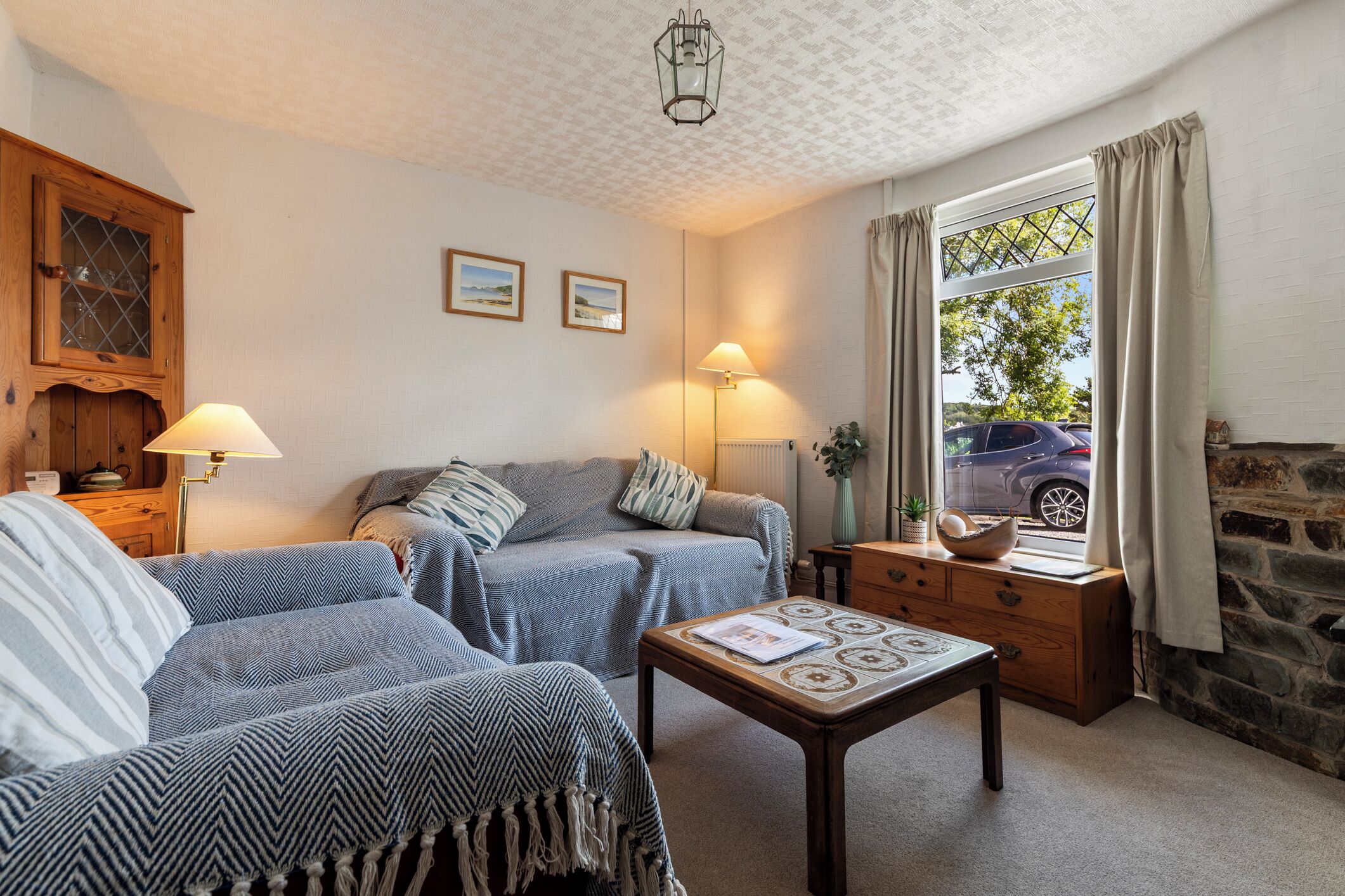 Una sala de estar acogedora con un sofá, un sillón y una mesita. Hay una ventana con cortinas, una lámpara y una chimenea de piedra.