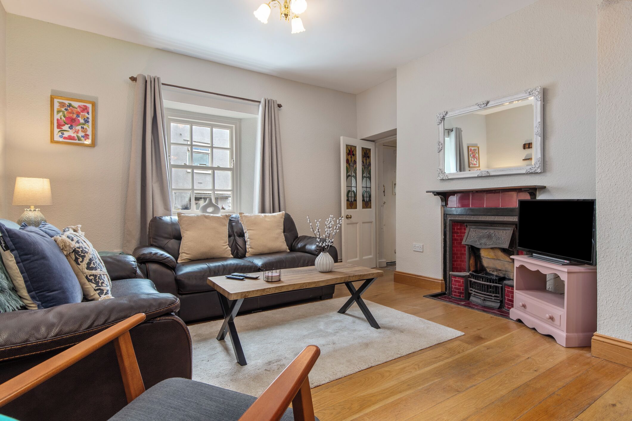 A living room with a leather sofa, a wooden coffee table, a television on a pink stand, and a fireplace.