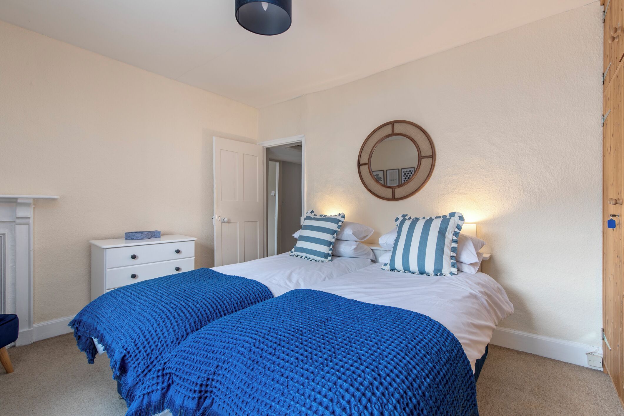 A bedroom with two beds, a white dresser, a round mirror, and a door leading to another room.