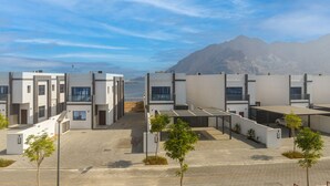 A modern building complex with multiple units, a paved courtyard, and a view of the sea and mountains in the background. - Sea Views & Private Pool, Near Beaches & Attractions – Sharm Al Dana (Fujairah)