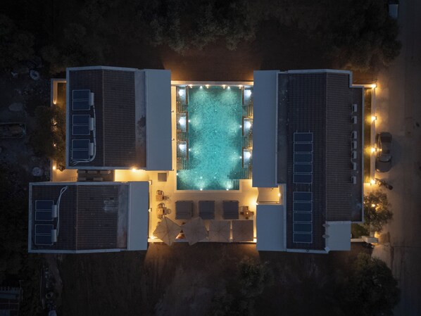 An aerial view of a hotel with a central swimming pool, multiple rooms with balconies, and a parking area.